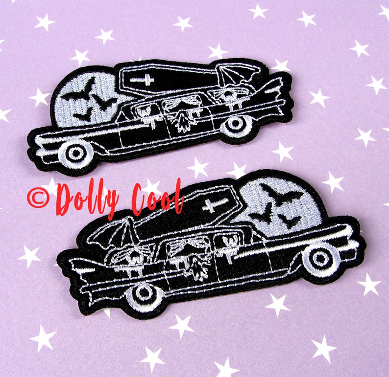 Pu&ograve; includere: Due toppe ricamate in bianco e nero raffiguranti un carro funebre con una bara, pipistrelli e una luna piena. Le toppe hanno un tema gotico e sono ambientate su uno sfondo viola con stelle bianche. Il testo "Dolly Cool" &egrave; in rosso.