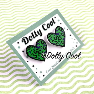 May include: A pair of green and purple heart-shaped earrings with a leopard print design. The earrings are on a white card with the text "Dolly Cool" and "Cool Jewels for Gals" in black.