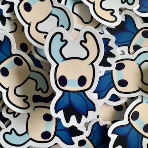 以下が含まれることがあります： クリーム色の顔、黒い目、青いマスクをした漫画のキャラクターのステッカーのコレクション。キャラクターは大きく湾曲した角と青と黒のマントを持っています。ステッカーは白い背景にあります。