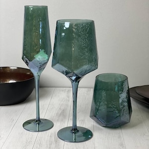 May include: Three teal green glass cups with a geometric design. The cups are on a white wooden surface.