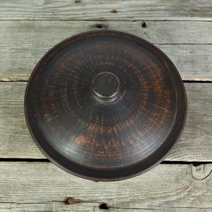 May include: A dark brown ceramic pot lid with a circular knob on top. The lid has a textured surface and a slightly raised rim.