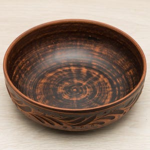 May include: A brown ceramic bowl with a dark brown glaze and a carved floral design around the rim.