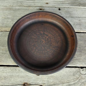 May include: A dark brown clay bowl with a smooth, slightly textured surface. The bowl is round and has a wide rim.