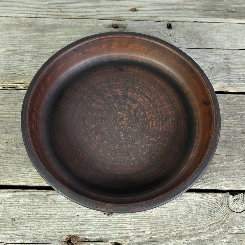 May include: A dark brown clay bowl with a smooth, slightly textured surface. The bowl is round and has a wide rim.