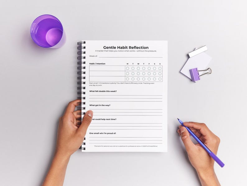 ADHD Habit Tracker printable page shown inside an open spiral-bound notebook, with a hand ready to write on it and a glass of water nearby.