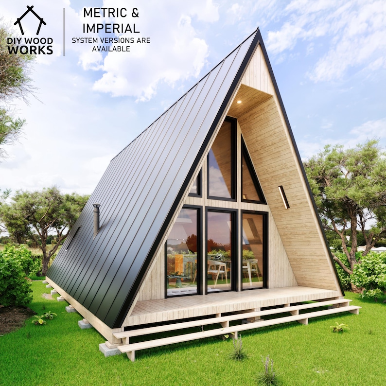 May include: A wooden A-frame house with a black metal roof and large windows. The house has a wooden deck and is surrounded by green grass.