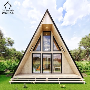 May include: A wooden A-frame house with large windows and a wooden deck. The house is surrounded by green grass and trees.