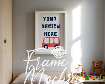 May include: A white picture frame with a red bus illustration and the text "YOUR DESIGN HERE" hanging on a light blue wall above a bed with a white pillow and a light brown wooden headboard. The room has a light brown wooden closet and a small table with toys on it.