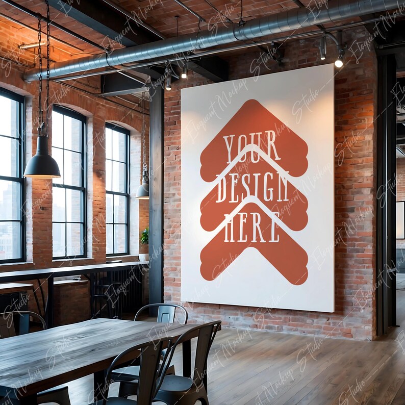 Op de afbeelding: Een wit canvas met de tekst "YOUR DESIGN HERE" in rood-oranje, gemonteerd op een bakstenen muur in een loft-achtige ruimte met een houten vloer en een tafel met stoelen.