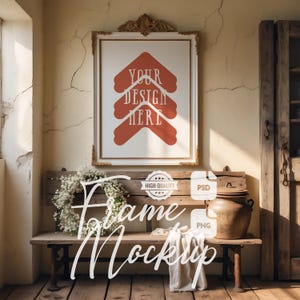 Puede incluir: Una maqueta de obra de arte enmarcada con el texto "YOUR DESIGN HERE" en naranja. El marco es dorado con detalles ornamentados. Un banco debajo sostiene una corona floral blanca, una manta y una olla rústica. Las palabras "Frame Mockup" están escritas en la imagen.