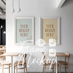 May include: Two framed art mockups with the text "YOUR DESIGN HERE" in a cafe setting. The frames are white, and the background colors are light blue and beige. The scene includes wooden tables, chairs, and hanging lights.