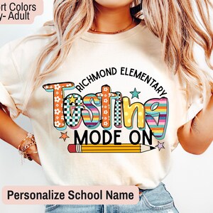 May include: Ivory-colored adult t-shirt with the words "Richmond Elementary Testing Mode On" in colorful, playful lettering. A pencil graphic is below the text. The shirt is a comfort color.