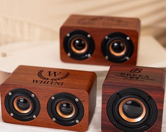 Puede incluir: Tres altavoces de madera con conos de altavoz negros y cobrizos. Los altavoces son rectangulares y tienen texto grabado. Uno tiene el nombre "WHITNI" y una "W" con hojas de laurel. Otro tiene el nombre "BREEA" y la fecha "20.03.2025".