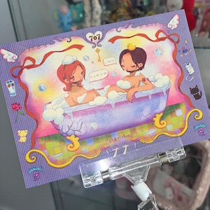 Pode incluir: Um cartão postal roxo com uma ilustração de duas pessoas numa banheira. O cartão tem uma borda decorativa com asas, fitas e texto japonês. O número 707 está no topo.