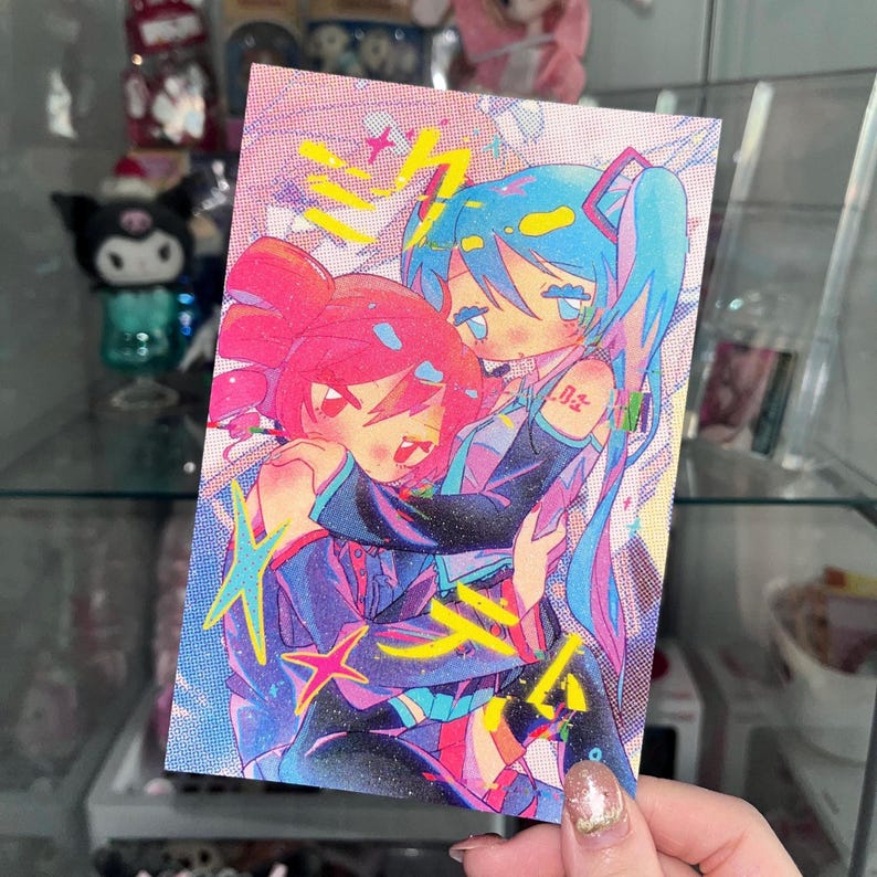 May include: A colorful postcard featuring two anime-style characters embracing. One character has pink hair, the other blue. The artwork has a vibrant, neon color palette with Japanese text and star accents.