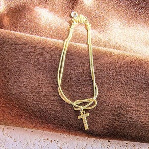 May include: A gold chain bracelet with a knot design and a small cross charm.