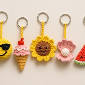 Op de afbeelding: Een rij van vijf gehaakte sleutelhangers. Ze tonen een gele smiley met zonnebril, een ijsje, een zonnebloem, een schelp met een parel en een watermeloen. Elke sleutelhanger heeft een metalen ring.