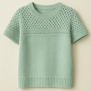 Op de afbeelding: Een lichtgroene, korte mouwen gebreide trui met een delicaat opengewerkt patroon rond de hals en schouders.