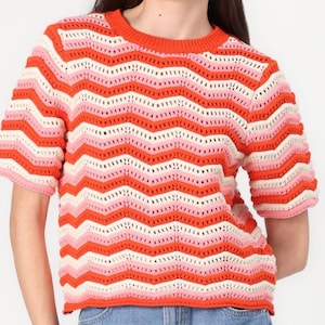 Op de afbeelding: Een korte mouwen, gebreide trui met een zigzagpatroon in tinten roze, wit en oranje.