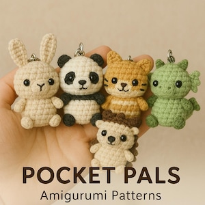 Op de afbeelding: Vijf gehaakte amigurumi dieren sleutelhangers: een wit konijn, een zwart-witte panda, een oranje-witte kat, een groene draak en een bruine egel. De sleutelhangers zijn in een rij gerangschikt en zijn gelabeld "Pocket Pals Amigurumi Patterns".
