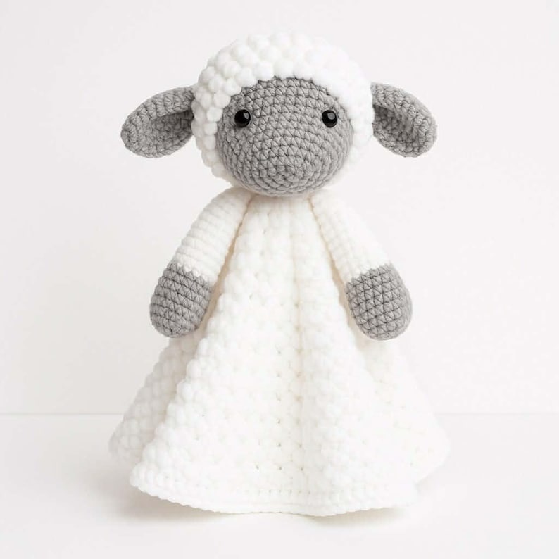 May include: A handmade crochet lamb toy. The lamb has a white body and head covering, with gray accents on the face, ears, and feet. The toy has a round head with black eyes and a soft, textured appearance.