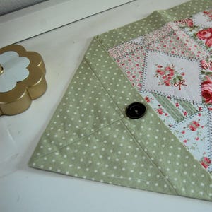 以下が含まれることがあります： 白のドット柄と花柄のパッチワークデザインの緑色のテーブルランナー。ランナーにはボタンのディテールがあり、どんなテーブルにも上品さを加えるのに最適です。