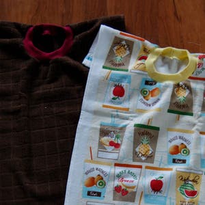 May include: Two brown kitchen towels, one with a red trim and the other with a blue trim and a colorful fruit print. The printed towel features a variety of fruits, including pineapples, strawberries, and watermelon.