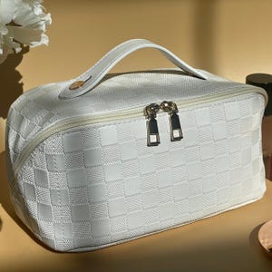 May include: White checkered makeup bag with a zipper closure and a top handle.