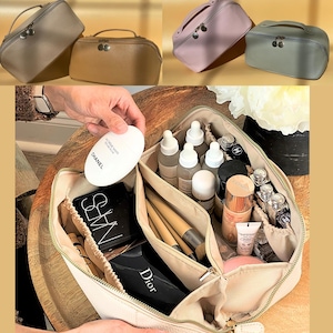 May include: A beige zippered travel makeup bag with multiple compartments, filled with various beauty products, including skincare, makeup, and brushes. The bag is open and the contents are visible. The bag is on a wooden surface.