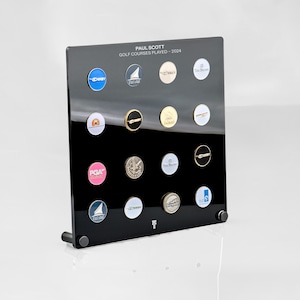 May include: Black display board with a white label that reads "PAUL SCOTT GOLF COURSES PLAYED - 2024". The board is filled with small round golf course markers with various logos and designs.
