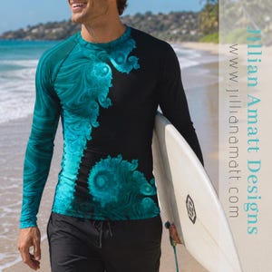 May include: A long-sleeve rash guard shirt featuring a black base with a vibrant teal fractal swirl pattern on the left side and sleeve. The text Jillian Amatt Designs and www.jillianamatt.com is printed vertically in teal on the right side.