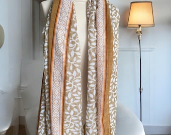 May include: A long rectangular scarf featuring a mustard yellow and white leaf pattern. The scarf includes vertical borders with a white and orange geometric diamond design, framed by solid mustard yellow stripes along the outer edges.