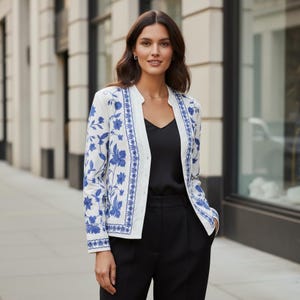 Può includere: Un blazer bianco a maniche lunghe con un vivace motivo floreale blu ricamato lungo i pannelli frontali e i polsini. Il blazer presenta un design senza colletto, aperto sul davanti con un orlo dritto, indossato sopra un top nero semplice.