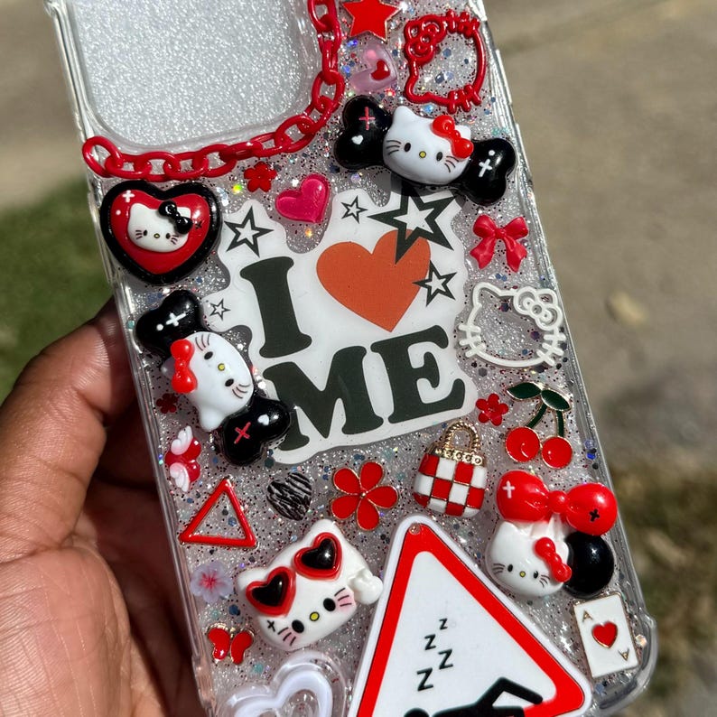 May include: Clear phone case decorated with various charms, including Hello Kitty figures, hearts, stars, and bows. The case features the words "I ❤️ ME" and a red chain. The design incorporates red, white, black, and glitter accents.