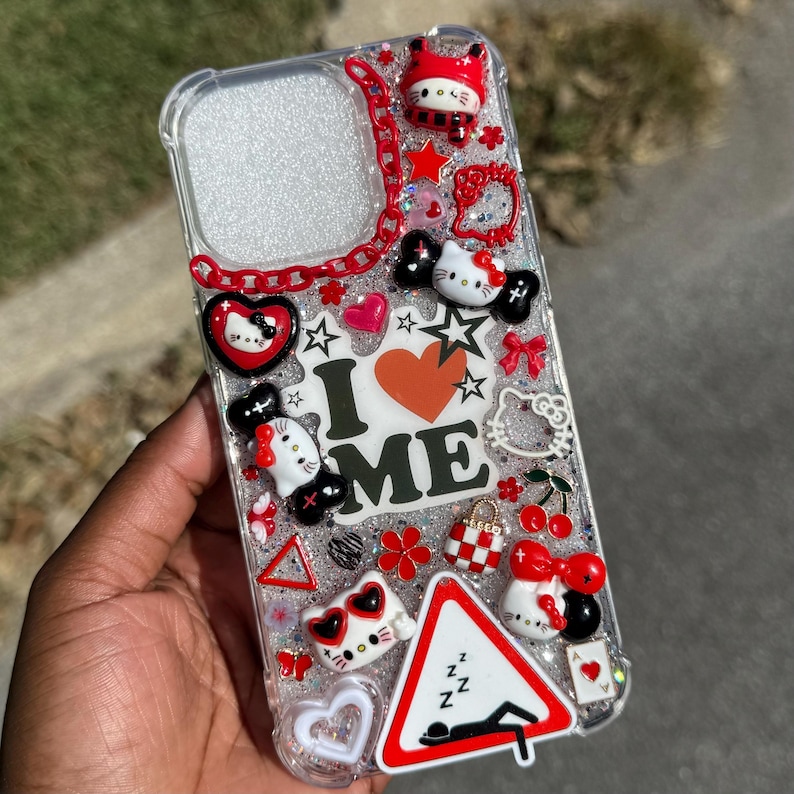 May include: Clear phone case decorated with various charms, including Hello Kitty figures, hearts, stars, and cherries. The case features the text "I ❤️ ME" and a red chain design. The case is filled with glitter.