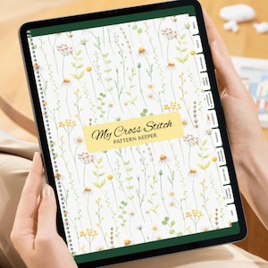 以下が含まれることがあります： 花柄のクロスステッチパターンキーパーを表示するデジタルタブレット。カバーには、黄色、緑、白のワイルドフラワーの水彩デザインが施されています。「My Cross Stitch Pattern Keeper」の文字が見えます。タブレットにはラベル付きのタブがあります。