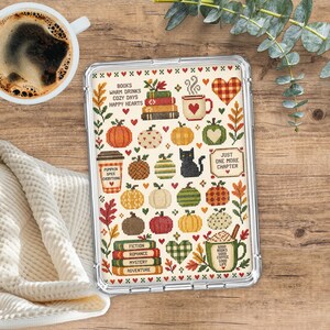 May include: A clear protective tablet case featuring a cross-stitch pattern of autumn motifs including pumpkins, stacked books, a black cat, and mugs. Text reads: BOOKS WARM DRINKS COZY DAYS HAPPY HEARTS, PUMPKIN SPICE EVERYTHING, JUST ONE MORE CHAPTER.