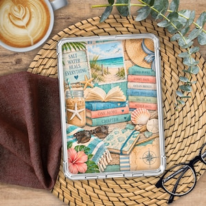 May include: A clear protective tablet case featuring a beach-themed illustration with a stack of books, a drink with a starfish, sunglasses, a straw hat, a compass, and a hibiscus flower. The text reads Salt Water Heals Everything.