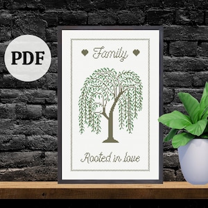 Può includere: Un'opera d'arte a punto croce incorniciata con un disegno di salice piangente. Le parole "Family" e "Rooted in love" sono ricamate in corsivo. L'opera d'arte è esposta su una mensola di legno contro un muro di mattoni neri.