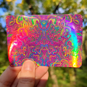 May include: A rectangular, iridescent card with a vibrant, psychedelic design. The artwork features swirling patterns in shades of pink, purple, yellow, green, and blue. The card's surface reflects light, creating a rainbow effect. The overall theme is abstract and artistic.