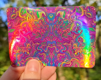 May include: A rectangular, iridescent card with a vibrant, psychedelic design. The artwork features swirling patterns in shades of pink, purple, yellow, green, and blue. The card's surface reflects light, creating a rainbow effect. The overall theme is abstract and artistic.