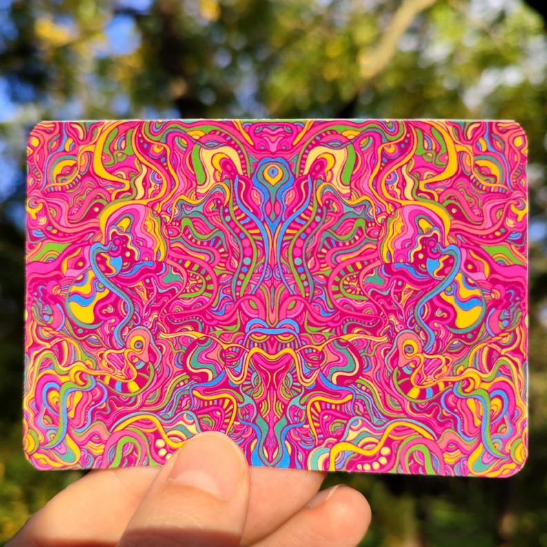 May include: A rectangular card with a vibrant, psychedelic design. The card features a complex pattern of swirling lines and shapes in shades of pink, yellow, green, blue, and purple. The design is symmetrical and visually striking, creating a sense of movement and depth.