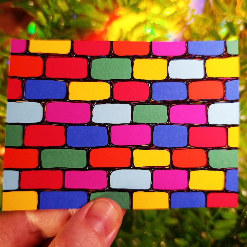 May include: A rectangular card featuring a colorful brick wall design. The bricks are in various colors, including red, yellow, blue, green, and pink, outlined in black. The card is held by a hand, with a blurred background.