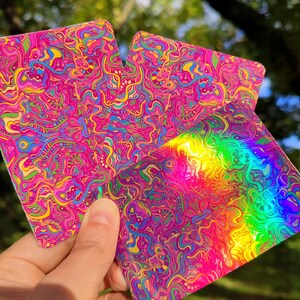 May include: Three colorful, square-shaped stickers with psychedelic designs. The stickers feature swirling patterns in shades of pink, blue, yellow, and green. One sticker has a rainbow gradient effect.