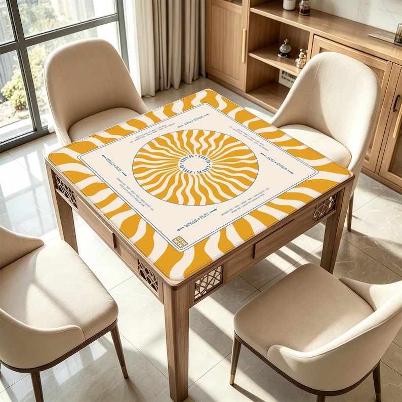 May include: A square wooden table with a cream-colored top featuring a yellow sunburst design. The table is surrounded by four beige chairs. The table has a drawer and decorative cutouts on the sides. The text on the table reads "Wills + Play".