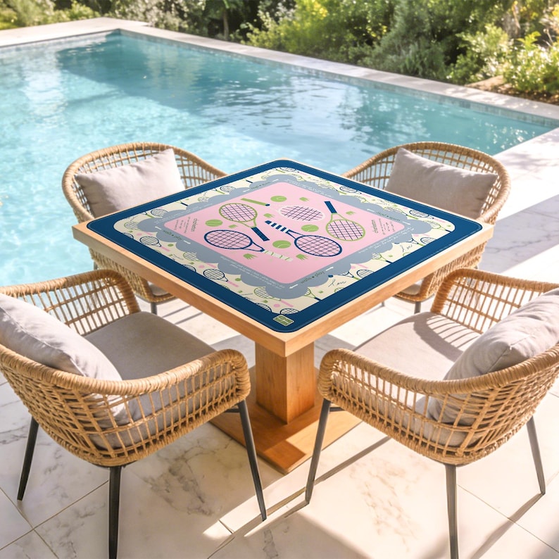 May include: A square wooden table with a pink tennis-themed design, surrounded by four wicker chairs with gray cushions. The table's design features tennis rackets and balls. The scene is set outdoors near a pool.