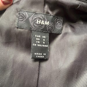 May include: Close-up of the interior lining of a black blazer. A black label with the H&M logo and size information is visible. The label indicates sizes EUR 36, US 6, and FR 6. The tag also states "MADE IN CHINA".
