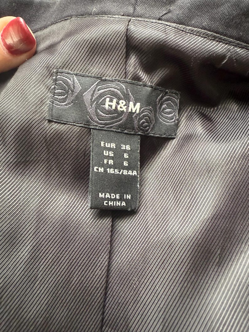 May include: Close-up of the interior lining of a black blazer. A black label with the H&M logo and size information is visible. The label indicates sizes EUR 36, US 6, and FR 6. The tag also states "MADE IN CHINA".
