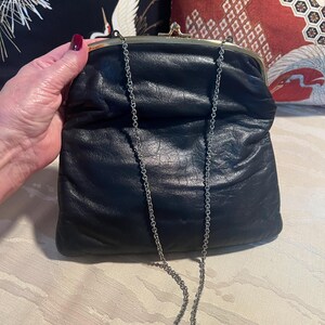 Pu&ograve; includere: Una pochette in pelle nera con una chiusura a scatto dorata e una tracolla a catena argentata.