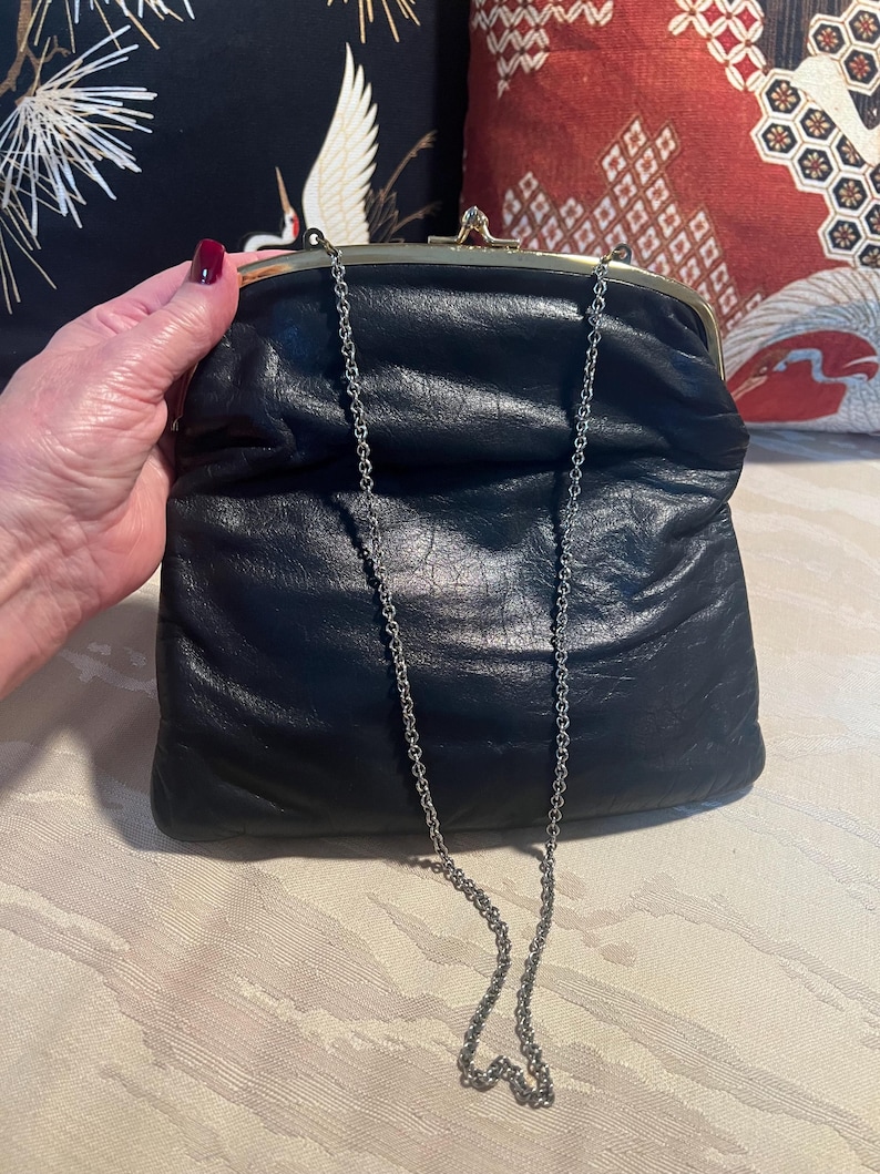 Pu&ograve; includere: Una pochette in pelle nera con una chiusura a scatto dorata e una tracolla a catena argentata.